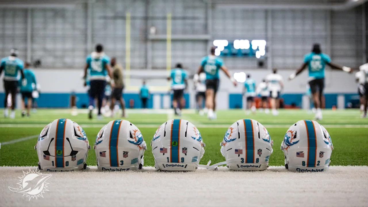 Miami Dolphins players warm up in the background, in the forefront are five player helmets