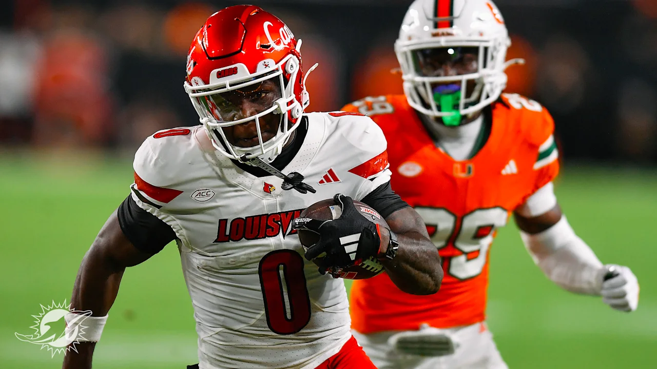 Louisville wide receiver in a white jersey, No. 0, sprints downfield carrying the football while being pursued by a Miami Hurricanes defender in an orange jersey, No. 89, during a college football game.